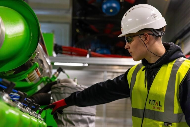 An engineer wearing a uniform and helmet inspects an electrical system