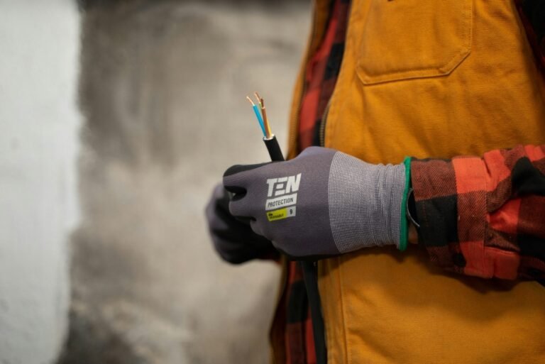 Electrician wearing protective gloves holding exposed electrical wires during installation work