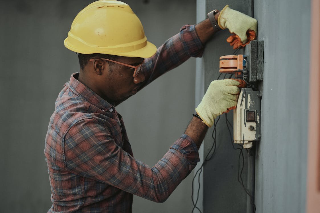 Electrician wearing a hard hat and gloves working on an exterior electrical box