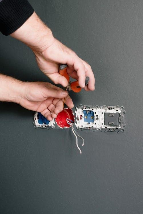 Electrician using tools to connect wires inside a wall outlet