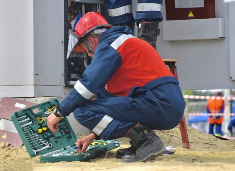 Technician in protective gear working on an outdoor electrical panel with tool kit